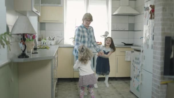 Бабушка танцует на кухне с двумя внучками. — стоковое видео