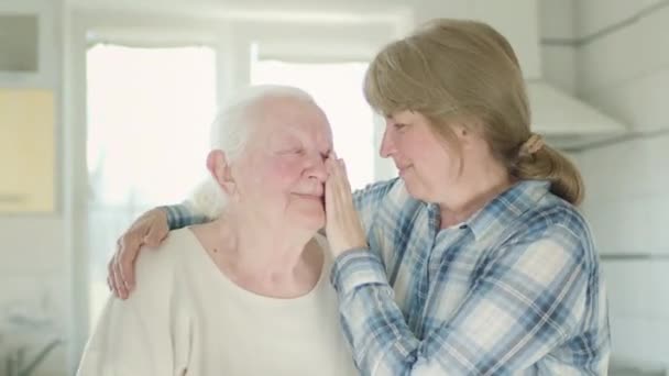 Portret van twee vrouwen. Dochter knuffelt haar oude moeder. Vrouwen in de keuken. — Stockvideo