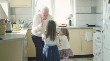 Yaşlı büyükanne mutfakta iki küçük torunuyla dans ediyor..
