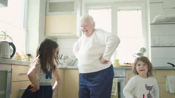 Vieja abuela bailando en la cocina con dos bisnietos. — Vídeo de stock