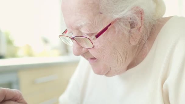 メガネの白髪のおばあちゃんは、ノートパソコンの画面で意図的に見えます. — ストック動画