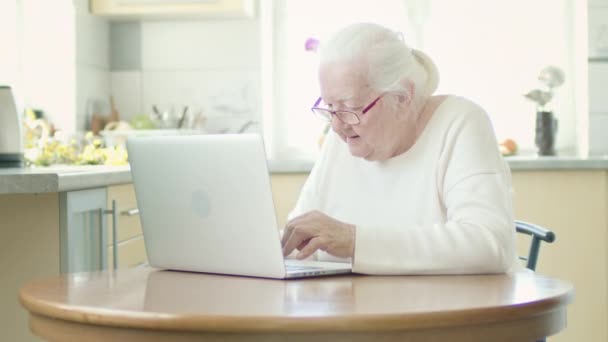 Grauhaarige Großmutter in Brille blickt gespannt auf den Laptop-Bildschirm. — Stockvideo