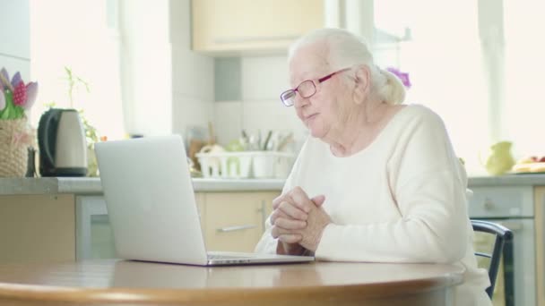 Gri saçlı gözlüklü büyükanne bilgisayar ekranına dikkatle bakıyor. Kadın video üzerinden biriyle konuşuyor.. — Stok video