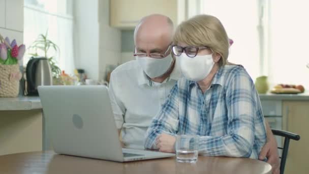 Мужчина и женщина в медицинских масках сидят за ноутбуком. Они общаются с кем-то через видео. — стоковое видео
