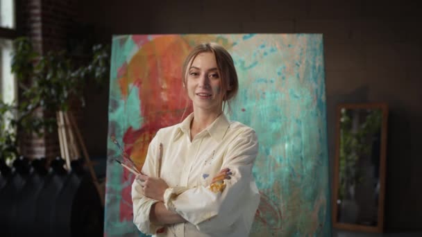 Jong meisje kunstenaar staande in de buurt van schilderen met borstels in haar handen. — Stockvideo
