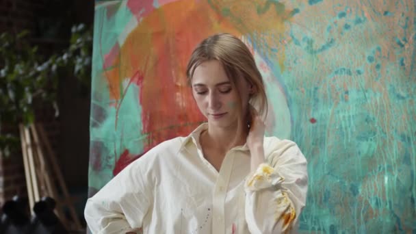 年轻的女艺术家站在绘画旁边. — 图库视频影像