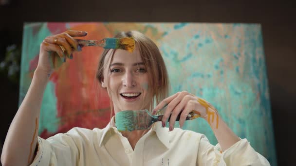 Fiatal lány tartja közel az arc ecsetek mártott festék. — Stock videók