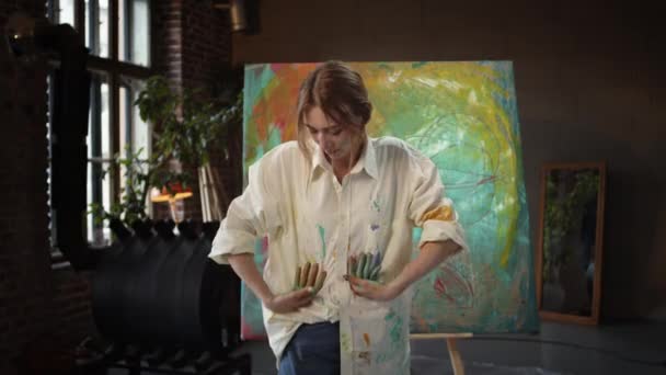 Jeune fille artiste dans le studio d'art. Elle essuie ses mains de la peinture dans sa chemise blanche. — Video