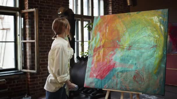 Девушка-художник в художественной студии. Она вытирает руки от краски в белой рубашке. — стоковое видео