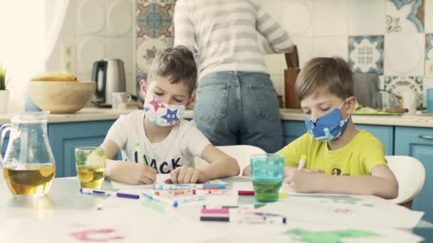 Dos chicos en máscaras médicas multicolores dibujan en la mesa en la cocina. — Vídeos de Stock