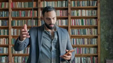 Kütüphanede elinde cep telefonu olan genç bir adam. Orta Doğu 'dan tatlı bir genç adam. Ceketli ve sakallı şık adam..