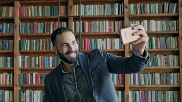 Joven en la biblioteca con teléfono móvil en sus manos. — Vídeos de Stock