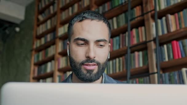 Стильный темноволосый парень с ноутбуком в комнате со многими книгами. — стоковое видео