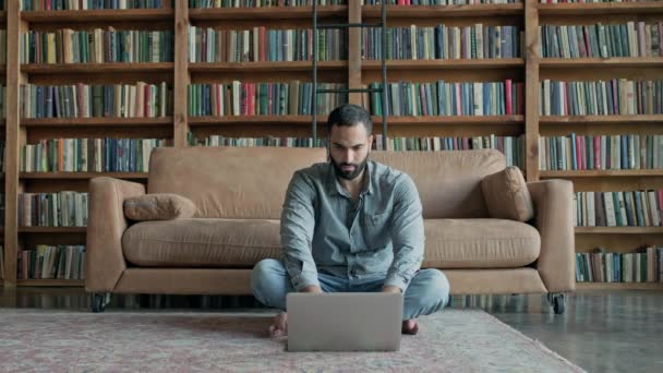 Stijlvolle jonge man zit op de vloer met laptop. — Stockvideo