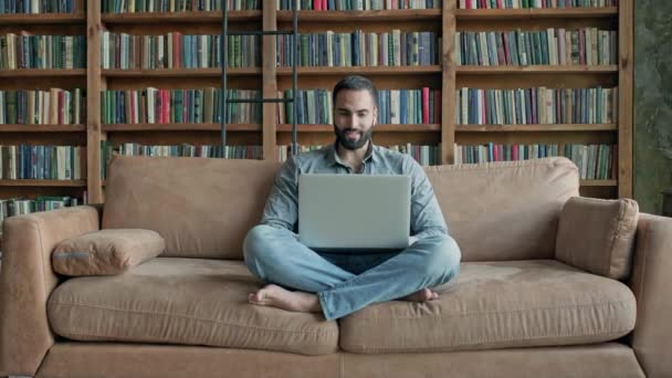 El tipo está sentado en el sofá y hablando a través de un ordenador portátil con alguien. — Vídeos de Stock