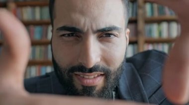 Ortadoğulu genç adam kütüphanede elleriyle kare çiziyor ve ona bakıyor..