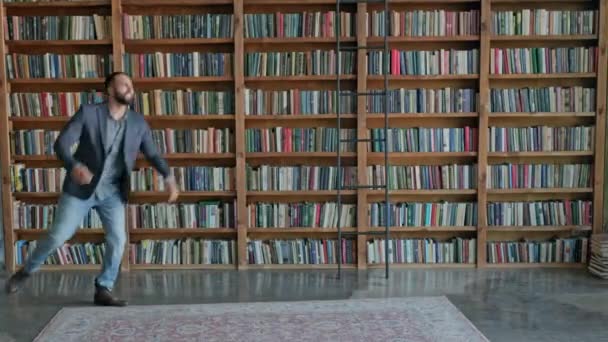 Młody człowiek skacze i raduje się w bibliotece. — Wideo stockowe