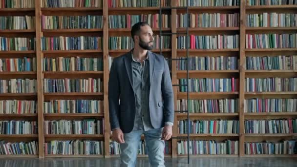 Killen står i biblioteket. Attraktiv brunett med skägg från Mellanöstern. — Stockvideo