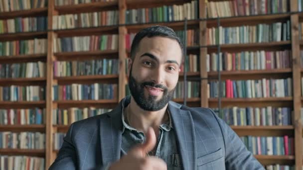 Elegante cara na biblioteca mostra com a mão que está tudo bem. — Vídeo de Stock