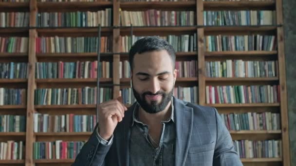 Joven con estilo escucha música a través de auriculares en la biblioteca. — Vídeo de stock