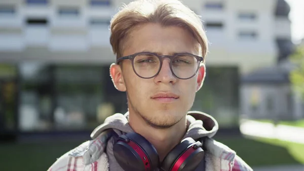 Portrait Of Young Guy On The Street. Handsome Guy In Glasses And Headphones Around His Neck.