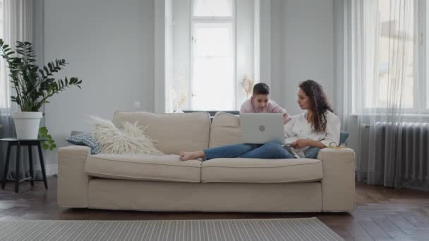 Unga mor och son. Ung kvinna som ligger på soffan med laptop. Vacker inredning i ljusa färger. — Stockvideo