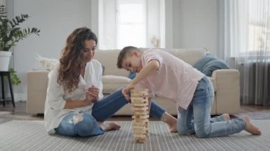 Anne ve Oğlu apartmanın zemininde oturuyorlar. Tahta Çubuklar Piramidi monte etme oyunu oynuyorlar..