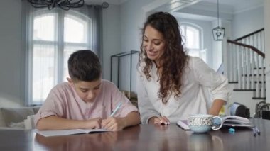 Masadaki genç anne ve oğlu. Oğlan Deftere Yazıyor. Ödevini yapıyor..