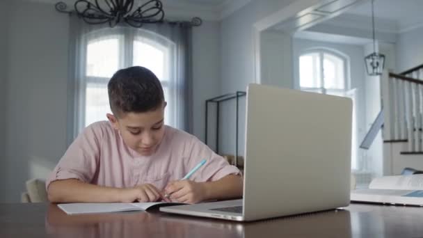 8岁的男孩坐在桌前的笔记本电脑前。他写在笔记本上。男孩做家务. — 图库视频影像