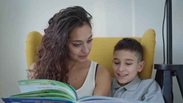 Giovane madre e figlio leggere libro insieme. Giovane bella donna con lunghi capelli ricci tenendo libro nelle sue mani. — Video Stock