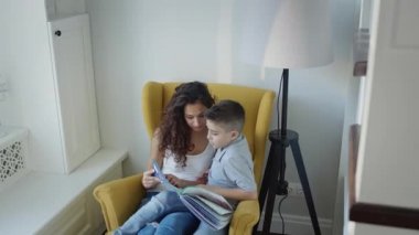 Genç anne ve oğlu birlikte kitap okuyor. Uzun kıvırcık saçlı, elinde kitap tutan genç ve güzel bir kadın..