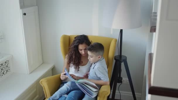 Jovem Mãe e Filho Leia Livro Juntos. Mulher bonita nova com cabelo encaracolado longo que prende o livro em suas mãos. — Vídeo de Stock