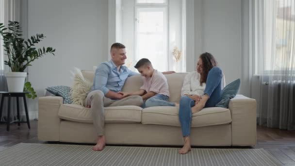 Glad ung familj på soffan i lägenheten. Pappa mamma och son skratta och ha kul. — Stockvideo