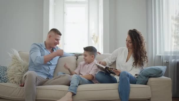 アパートのソファの上の幸せな若い家族。パパママと息子は笑って楽しんでる. — ストック動画