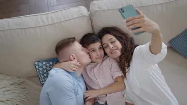 Mladá matka fotí svou rodinu na telefonu. Máma, táta a syn na gauči. Rodina baví. — Stock video