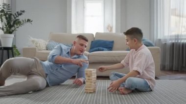 Baba ve Oğul apartmanda yerde oturuyorlar. Tahta Çubuklar Piramidi monte etme oyunu oynuyorlar..