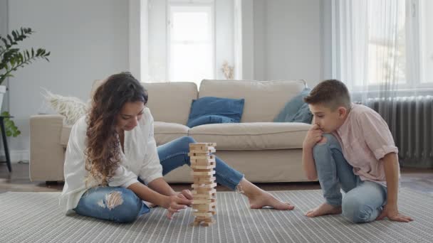 Мать и сын сидят на полу в квартире. They play Game Of Assembling Pyramid Of Wooden Bars. — стоковое видео