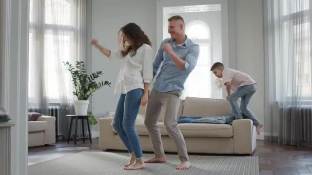 Lazer Jovem Família Pai e Mãe Dança No Quarto Descalço E Jovem Filho Salta No Sofá. — Vídeo de Stock