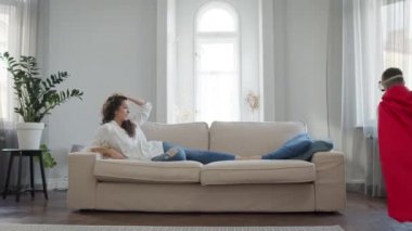 Anne ve Oğul odada. Kırmızı pelerinli ve gözlüklü çocuk Superman 'i oynuyor..