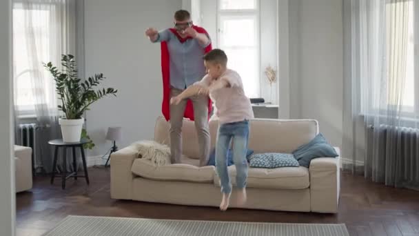 Vader en zoon in het appartement spelen spel. Vader in rode mantel en bril vertegenwoordigt Superman. — Stockvideo