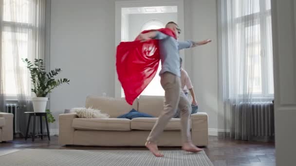 Pai e filho no apartamento a jogar. Pai em manto vermelho e óculos Depicts Superman. — Vídeo de Stock