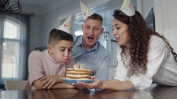 Vader, moeder en zoon vieren hun verjaardag. Moeder houdt taart vast en zoon blaast de kaarsen uit. — Stockvideo