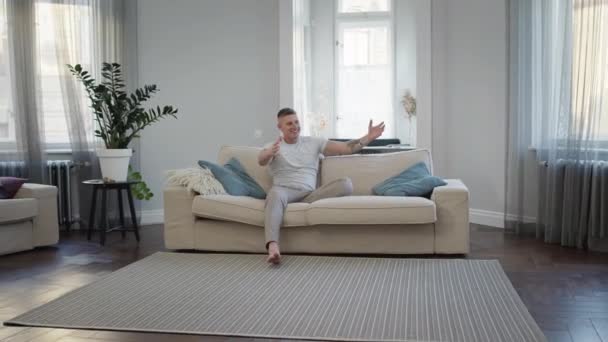 Hombre joven sentado en el sofá en el apartamento. Su hijo corre hacia él. — Vídeos de Stock