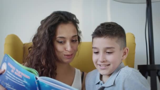 Młoda matka i syn czytają książkę razem. Młoda ładna kobieta z długimi kręconymi włosami trzymając książkę w rękach. — Wideo stockowe