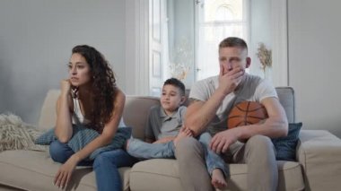 Odadaki koltukta oturan genç bir aile. Televizyon izleyip spor oyunları için tezahürat yapıyorlar..