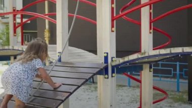Oyun parkındaki küçük kız. Kız dizlerinin üstüne çöker ve elleri oyundan çekilir ve kurtulur. Uzun kıvırcık saçlı güzel kız..