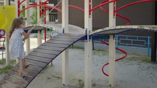 Kleines Mädchen auf dem Spielplatz. Hübsches Mädchen mit langen lockigen Haaren. — Stockvideo