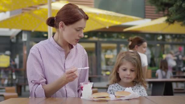 Joven madre y niña en el café comiendo helado. Madre alimenta a su hija con cuchara. — Vídeos de Stock