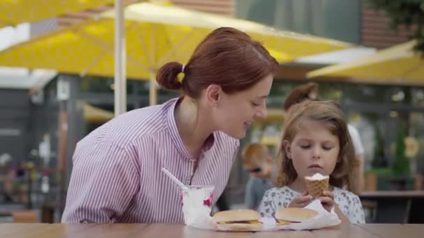 Giovane madre e bambina nel caffè mangiare gelato. Donna che fa il tifo per il bambino. Sembra che voglia mangiare il gelato delle ragazze.. — Video Stock