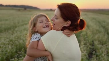 Genç Anne, kızını kollarında tutuyordu. Arazinin ortasındalar. Anne kızını öpüyor..